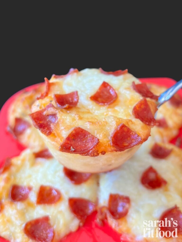 keto pizza muffin shown with a tray of pizza muffins behind it