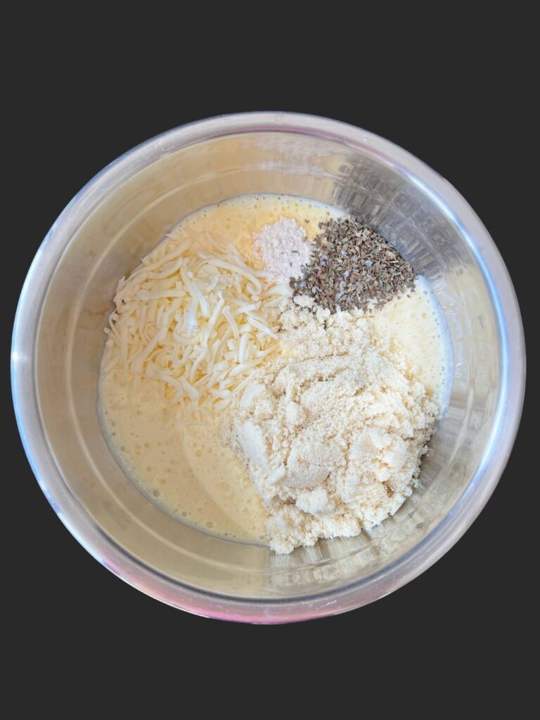 ingredients shown in a bowl before mixing, including blended eggs and cottage cheese, almond flour, mozzarella cheese, and spices.