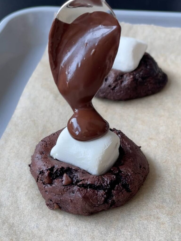 spooning melted chocolate over top of the marshmallows